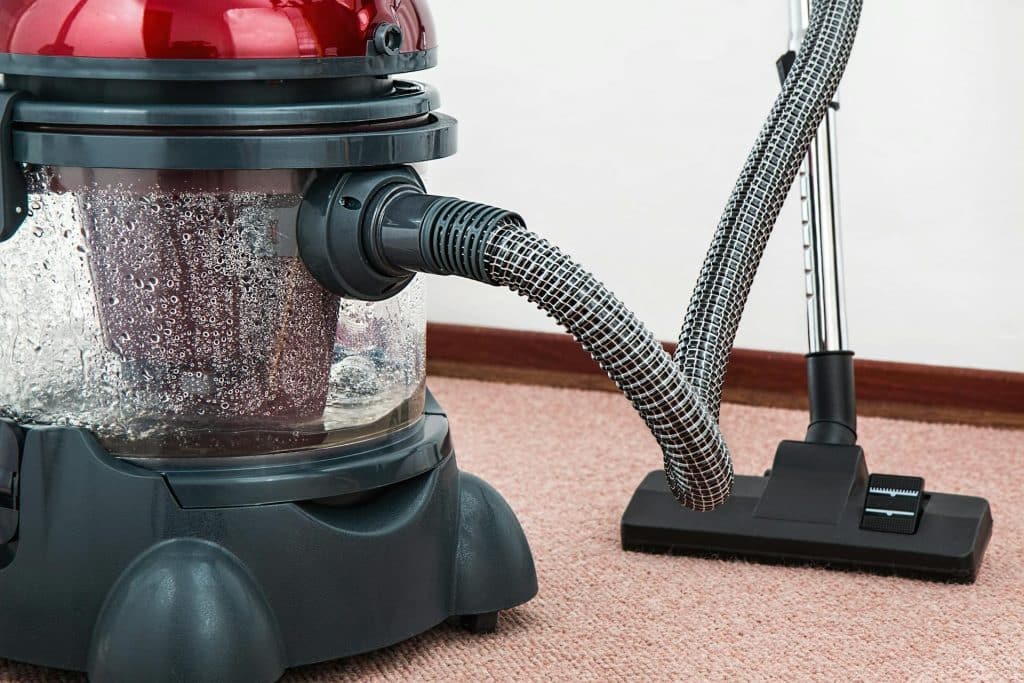 Red vacuum cleaner with a transparent water container on carpeted floor.